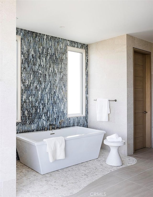 bathroom featuring tile patterned floors, a tub to relax in, and tile walls