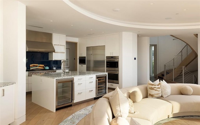 kitchen with white cabinetry, beverage cooler, appliances with stainless steel finishes, and a center island with sink