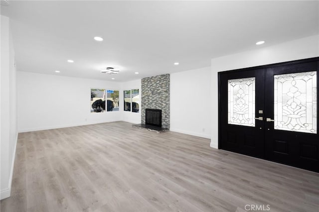 unfurnished living room featuring a stone fireplace, light hardwood / wood-style flooring, and french doors