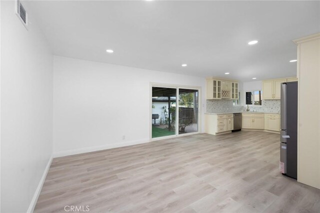 kitchen featuring cream cabinets, decorative backsplash, stainless steel appliances, and light wood-type flooring