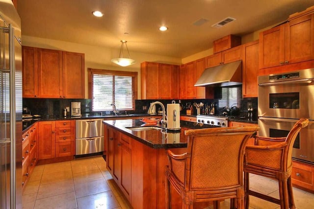 kitchen featuring sink, extractor fan, appliances with stainless steel finishes, pendant lighting, and a kitchen island with sink