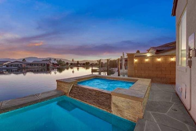 pool at dusk with a water view and an in ground hot tub