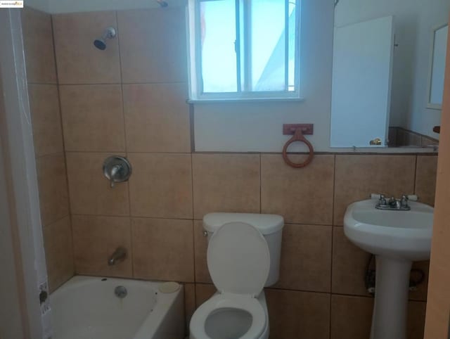 bathroom with tiled shower / bath, toilet, and tile walls