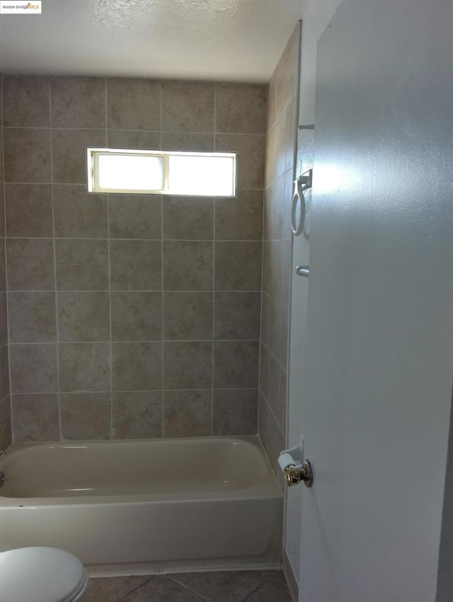 bathroom featuring tiled shower / bath, tile patterned floors, toilet, and a textured ceiling