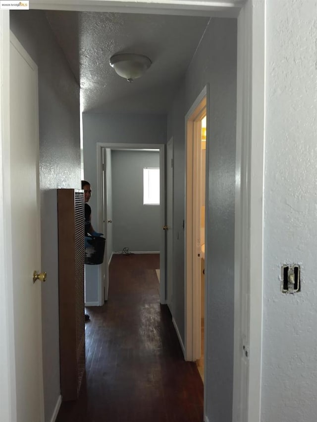 corridor with a textured ceiling and dark hardwood / wood-style flooring