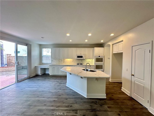 kitchen featuring white cabinetry, an island with sink, double oven, and light stone counters