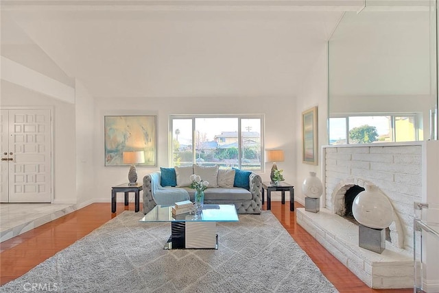 living room featuring lofted ceiling, a brick fireplace, and wood-type flooring