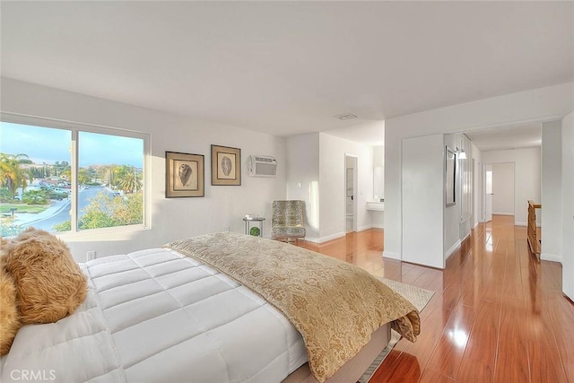 bedroom with a wall mounted air conditioner, light wood-type flooring, and ensuite bathroom