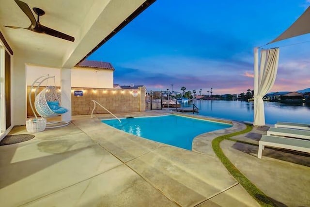 pool at dusk with a water view, ceiling fan, and a patio area