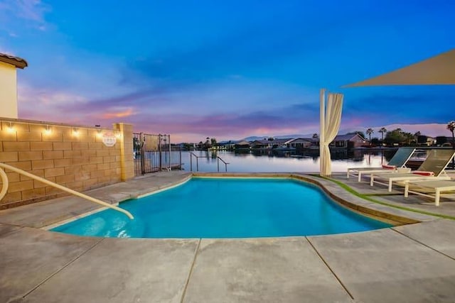 pool at dusk featuring a patio and a water view