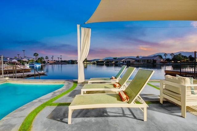 pool at dusk with a water view, a dock, and a patio