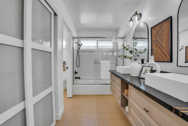 full bathroom featuring toilet, combined bath / shower with glass door, a textured ceiling, vanity, and hardwood / wood-style floors