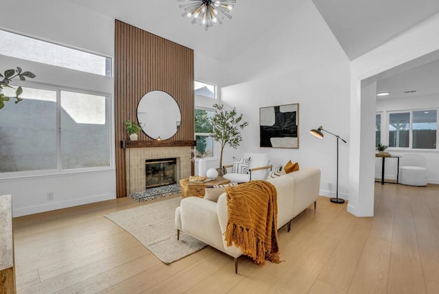 living room with a tiled fireplace, a high ceiling, a chandelier, and light hardwood / wood-style flooring