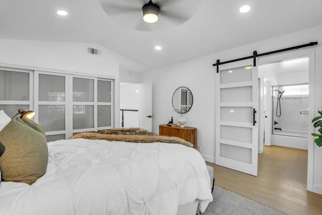 bedroom with ceiling fan, lofted ceiling, a barn door, and light hardwood / wood-style flooring