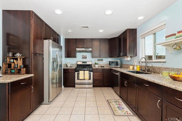 kitchen with appliances with stainless steel finishes, sink, light tile patterned floors, light stone counters, and dark brown cabinets