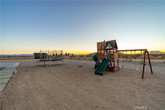 playground at dusk featuring a mountain view and a trampoline