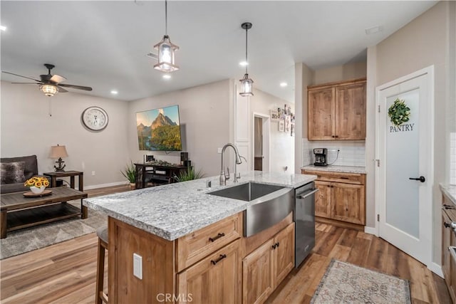 kitchen featuring dishwasher, sink, decorative backsplash, hanging light fixtures, and a kitchen island with sink