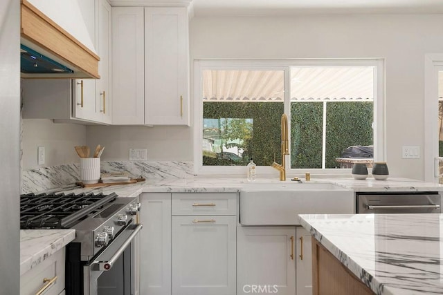 kitchen with sink, white cabinets, custom exhaust hood, high end stainless steel range, and light stone counters