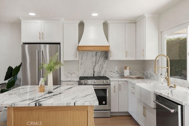 kitchen with a kitchen island, white cabinetry, appliances with stainless steel finishes, and custom range hood