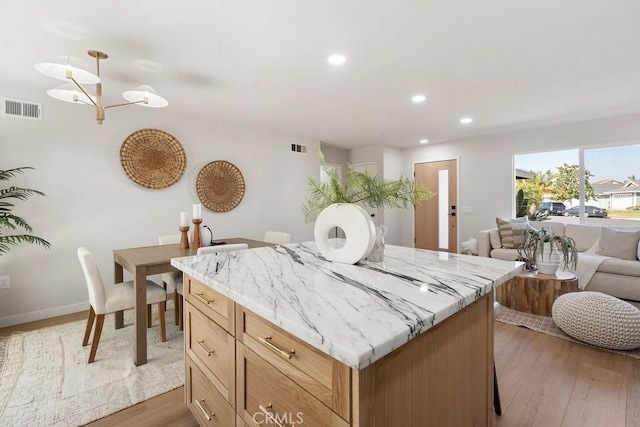 kitchen with light stone countertops, wood-type flooring, a kitchen island, and decorative light fixtures