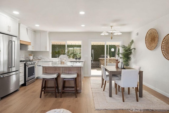 kitchen with white cabinetry, light stone counters, premium appliances, a kitchen island, and custom range hood