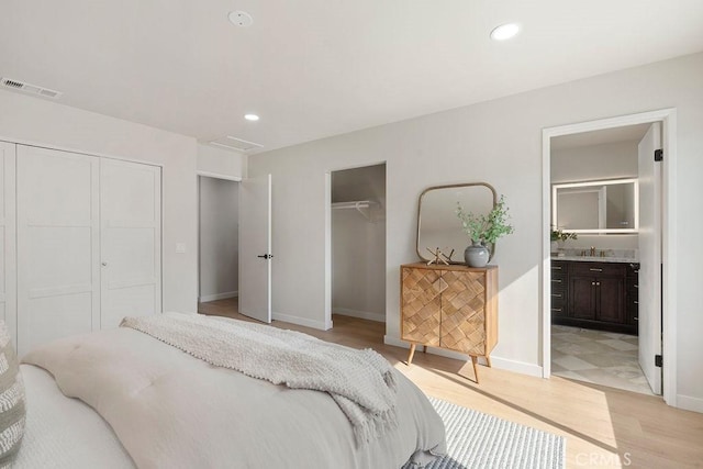 bedroom with sink, two closets, light hardwood / wood-style floors, and ensuite bathroom