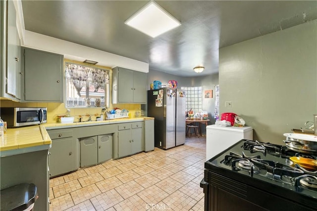 kitchen featuring stainless steel appliances, green cabinets, sink, and tile counters