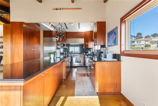 kitchen featuring sink, built in appliances, extractor fan, and light wood-type flooring