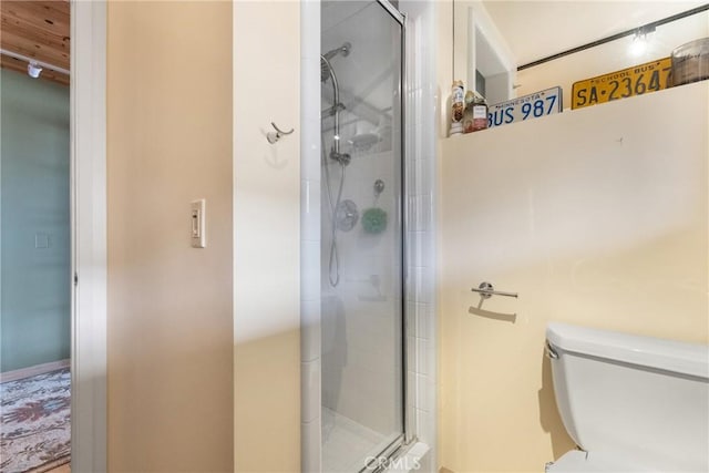 bathroom featuring a shower with door and toilet