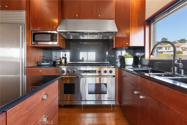 kitchen featuring dark wood-type flooring, sink, high end appliances, range hood, and decorative backsplash