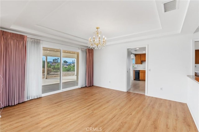 unfurnished living room with a tray ceiling, a notable chandelier, and light hardwood / wood-style flooring