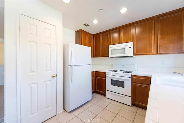 kitchen with light tile patterned flooring, white appliances, tile countertops, and sink