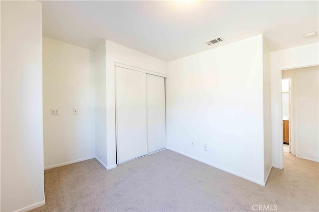 unfurnished bedroom with light colored carpet and a closet