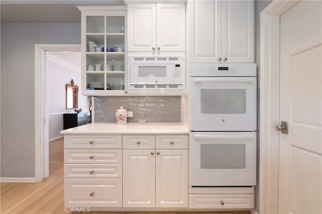 kitchen with white cabinetry, light wood-type flooring, backsplash, and white appliances