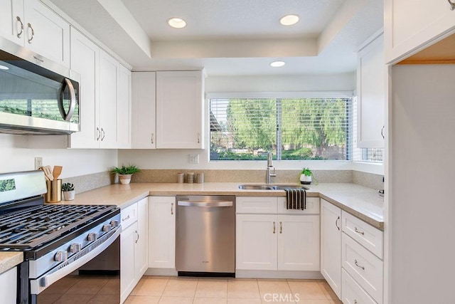 kitchen featuring light tile patterned flooring, sink, white cabinetry, appliances with stainless steel finishes, and a tray ceiling