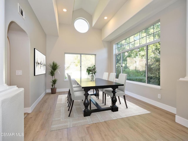 dining space with light hardwood / wood-style flooring, high vaulted ceiling, and ornate columns