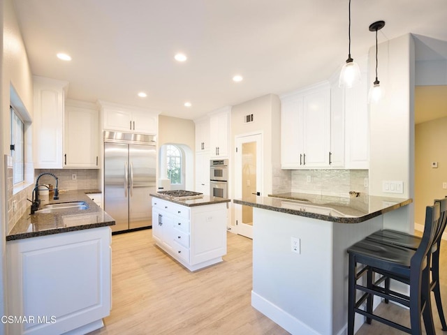 kitchen featuring a kitchen island, appliances with stainless steel finishes, white cabinetry, sink, and light hardwood / wood-style floors