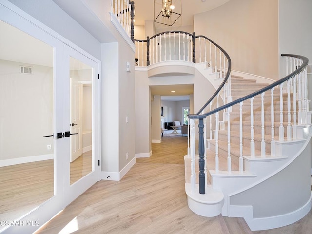 entrance foyer featuring french doors, a towering ceiling, a chandelier, and hardwood / wood-style floors