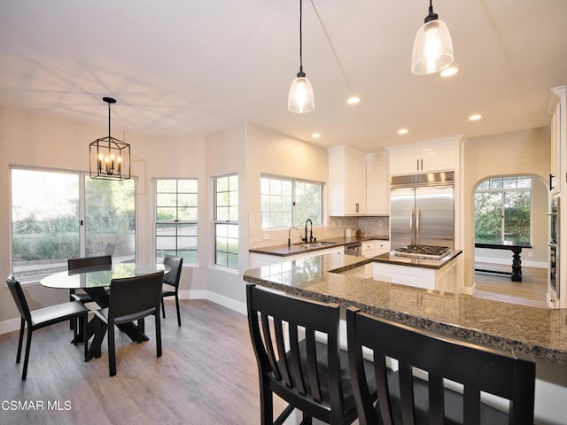 kitchen featuring tasteful backsplash, white cabinetry, appliances with stainless steel finishes, and decorative light fixtures