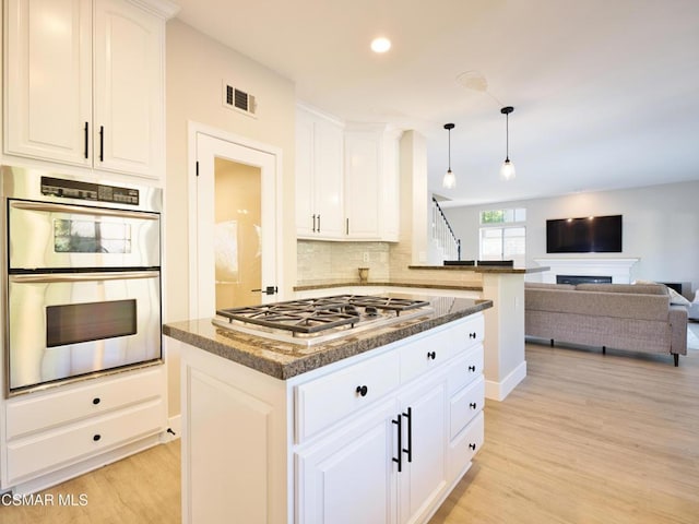 kitchen with light hardwood / wood-style flooring, appliances with stainless steel finishes, white cabinetry, dark stone countertops, and a center island