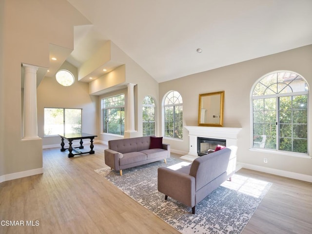 living room with decorative columns, light wood-type flooring, and high vaulted ceiling