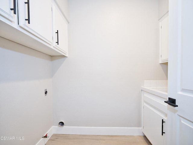 washroom featuring cabinets, hookup for an electric dryer, light hardwood / wood-style floors, and hookup for a gas dryer