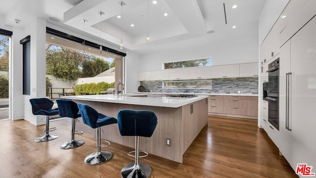 kitchen featuring a spacious island, a breakfast bar, decorative backsplash, and white cabinets