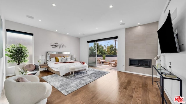 bedroom featuring a tiled fireplace, hardwood / wood-style flooring, and access to outside