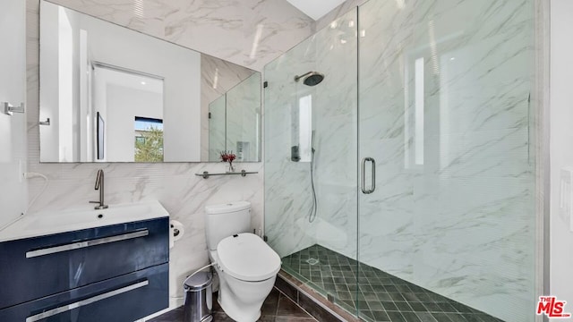 bathroom with vanity, toilet, a shower with shower door, and tile walls