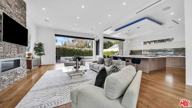 living room with a tray ceiling, a stone fireplace, and light wood-type flooring