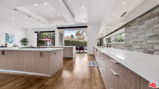 kitchen with a spacious island, sink, tasteful backsplash, decorative light fixtures, and light wood-type flooring