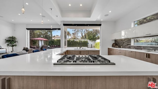 kitchen with pendant lighting, stainless steel gas stovetop, white cabinetry, sink, and decorative backsplash