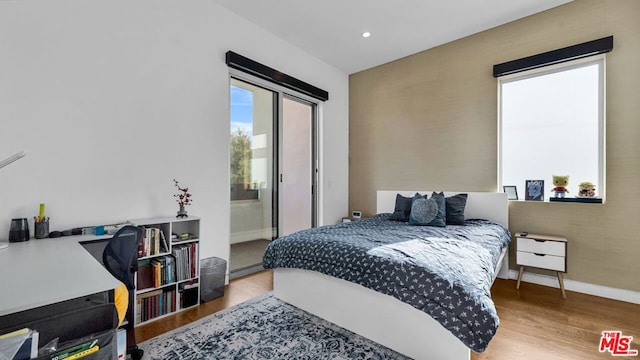 bedroom featuring access to exterior, hardwood / wood-style floors, and a baseboard heating unit