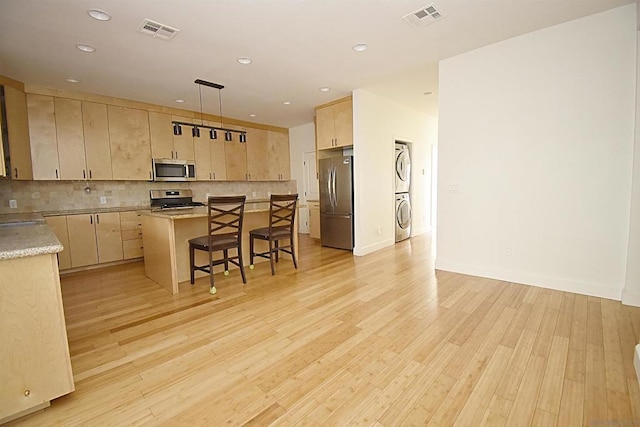 kitchen with a breakfast bar, stainless steel appliances, a center island, stacked washer / drying machine, and decorative light fixtures